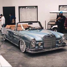 an old car parked in a garage with people standing around and looking at the cars