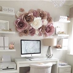 a white desk topped with a computer monitor next to a wall covered in paper flowers