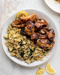 a white plate topped with chicken and rice next to lemon wedges on a table