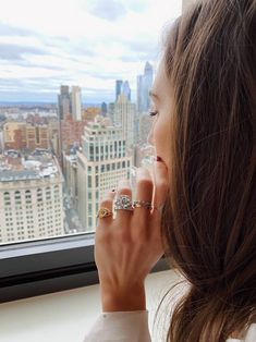 a woman is looking out the window with her hand on her chin and wearing rings