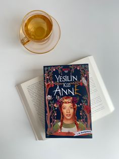 a cup of tea sits next to an open book and a glass of tea on a white surface