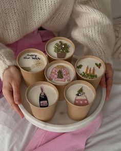 a woman is holding a tray full of small cups with embroidered designs on the sides