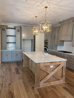 a large kitchen with an island in the middle and two chandeliers hanging from the ceiling