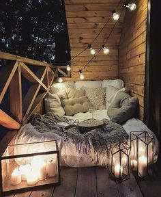 a bed sitting on top of a wooden floor covered in blankets and pillows next to lit candles