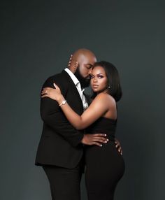 a man and woman embracing each other in front of a dark background with their arms around each other