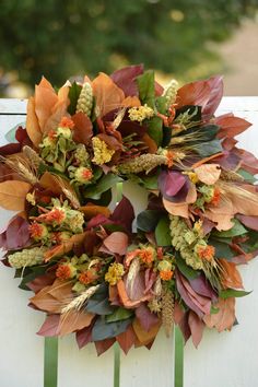 a wreath with leaves and flowers on a white fence