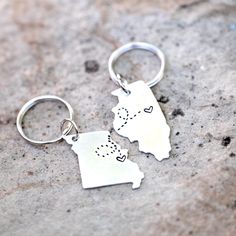 two metal key chains with the shape of michigan and heart on them sitting on a stone surface