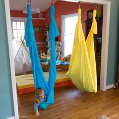 a toddler is sitting in a hammock with blue and yellow drapes hanging from the ceiling