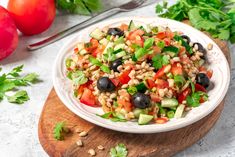 a white bowl filled with salad sitting on top of a wooden cutting board next to tomatoes