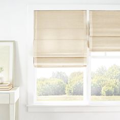 a white room with two windows covered in roman shades and a mirror on the wall