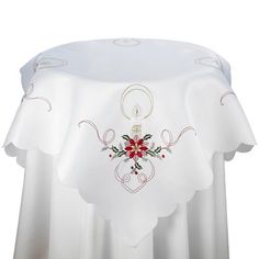 a white table cloth with red flowers on it and a candle in the center,