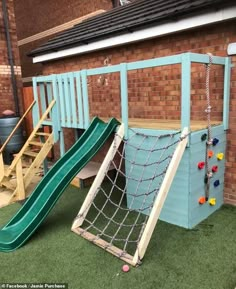 a play area with a slide and climbing wall in front of a brick building on artificial grass