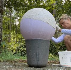 a woman sitting on the ground next to a bucket with a large ball in it