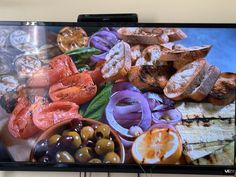 a flat screen tv sitting on top of a wooden table next to a bowl of fruit and veggies