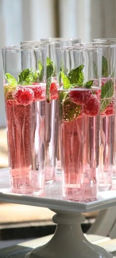 four glasses filled with water and raspberries on top of a table next to each other