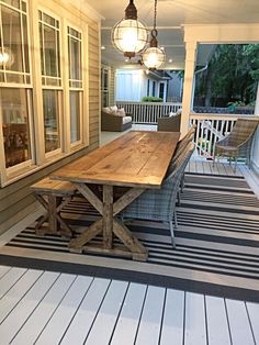 a wooden table sitting on top of a porch next to a white house with lots of windows