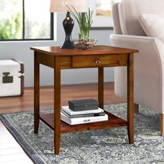 a small wooden table with a lamp and books on it in a living room area