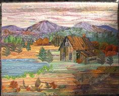 a quilted wall hanging with a house and mountains in the background