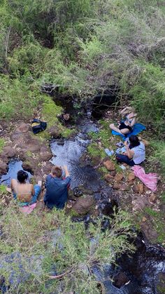 two people sitting on the ground next to a stream