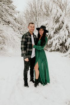 a man and woman are standing in the snow together, one is wearing a green dress