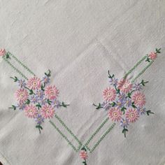 two pink flowers on white linen with green stems and purple daisies in the center