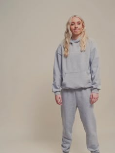 a woman standing in front of a white background wearing a grey sweatshirt and sweatpants