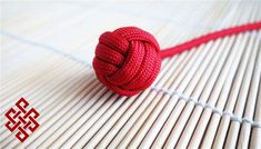 a red knoted ball sitting on top of a bamboo mat next to a string