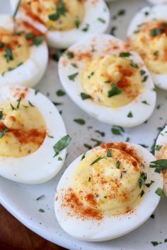 deviled eggs with herbs and seasoning sit on a white plate, ready to be eaten