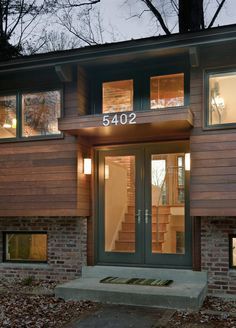 the front entrance to a modern home with wood siding and glass doors at night time