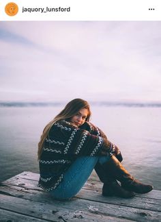 a woman sitting on top of a wooden dock next to the ocean