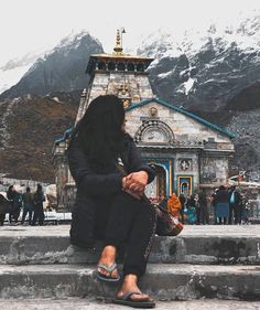 a woman sitting on steps in front of a building with snow covered mountains behind her