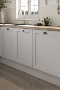 a kitchen with white cabinets and wooden counter tops next to a potted plant on the window sill