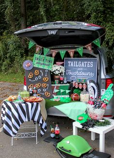 an outdoor tailgate party with green and black decorations, food and drinks in the trunk