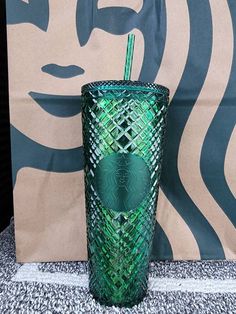 a green starbucks cup with a straw in front of a large wallpapered background