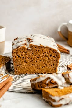 a loaf of pumpkin bread with icing on a cooling rack next to cinnamon sticks