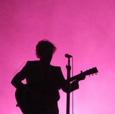 the silhouette of a person playing an acoustic guitar in front of a microphone and pink background