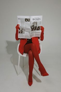 a woman sitting in a white chair while reading a newspaper with red stockings and heels