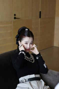 a woman sitting on top of a couch wearing a black sweater and pearl necklaces