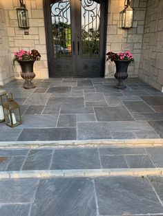 two vases with flowers sit on the front steps of a house that is decorated in stone