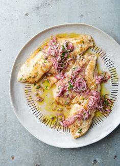 a white plate topped with fish covered in sauce and onions on top of a table