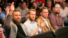 a group of men sitting next to each other in front of a crowd with their hands up