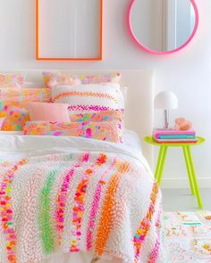 a white bed topped with lots of pillows and blankets next to a pink wall mounted mirror