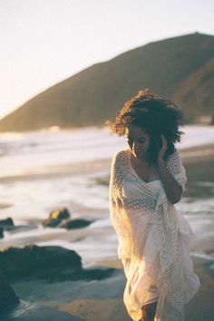 a woman is walking on the beach talking on her cell phone while wearing a white dress