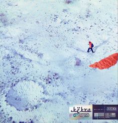 a man walking across a snow covered field next to an orange kite in the air