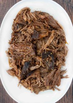 shredded meat on a white plate sitting on top of a wooden table