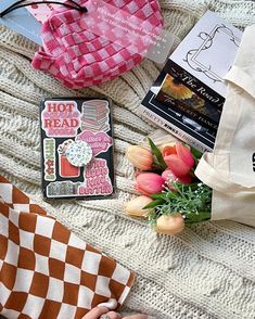 the contents of a handbag are laid out on a blanket with flowers and books