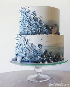 a three tiered cake with blue and white icing on a glass platter