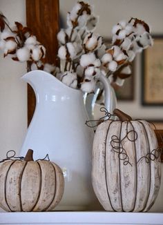 two white pumpkins sitting on top of a shelf next to a vase with cotton flowers