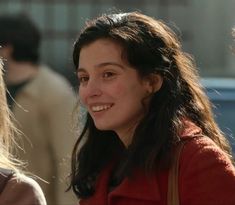 a woman with long hair smiles at the camera while standing next to another woman wearing a red coat