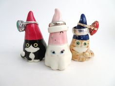 three small figurines with cats wearing hats on their heads and eyes, all in different colors